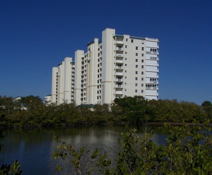 Photo of a large, white condo building surrounded by trees and water.