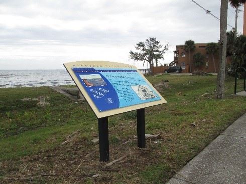 Photo of a dark/light blue graphic panel with text, sitting along the river.